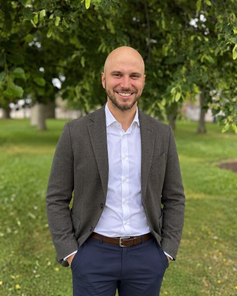 Ondrej Stafa im Freien vor grünen Bäumen, in dunklem Sakko und weissem Hemd.